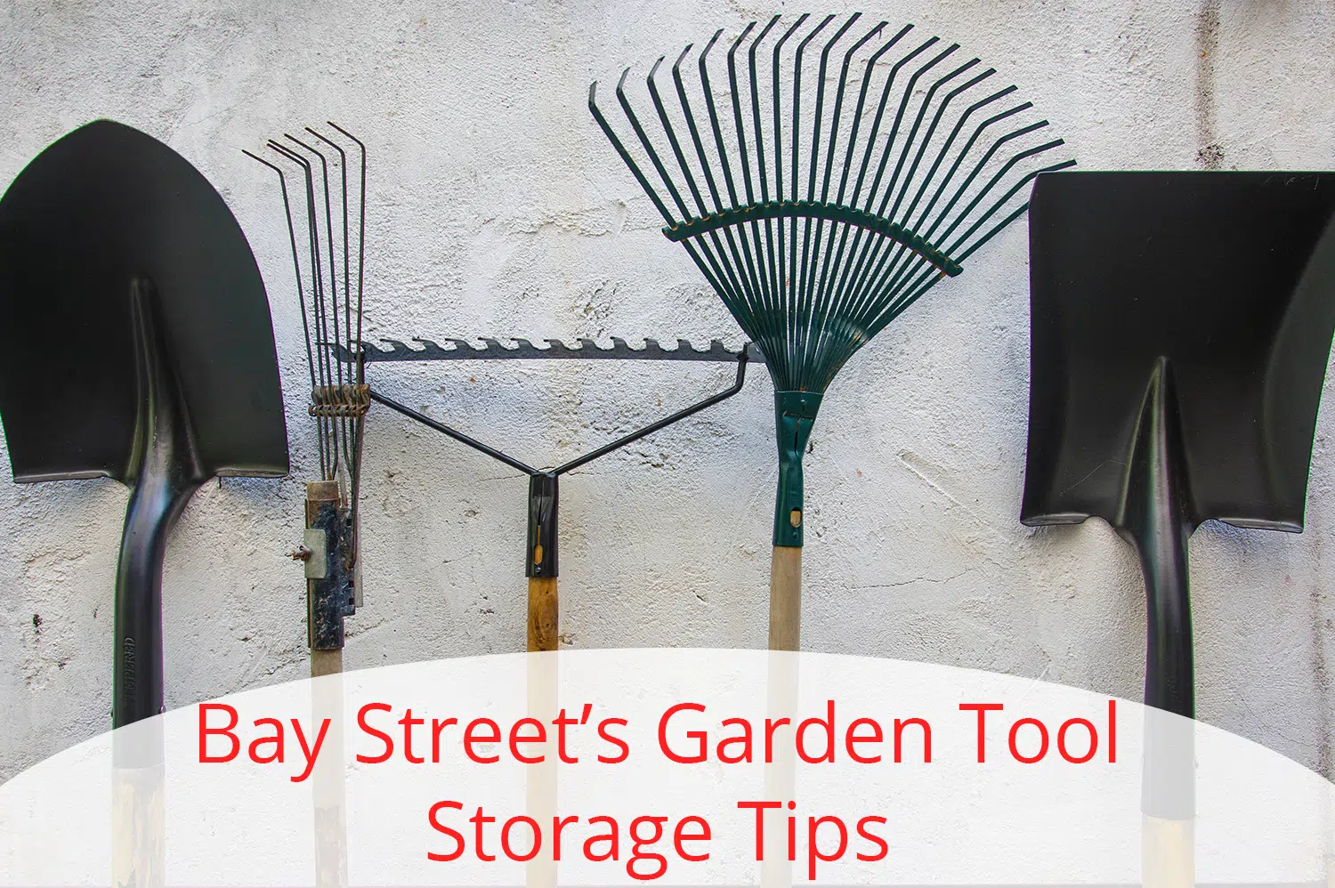 Two shovels and three rakes lined up on a white wall getting ready for garden tool storage.